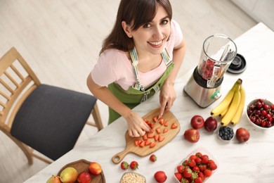 Photo of Young woman making delicious smoothie with blender at white marble table in kitchen, above view