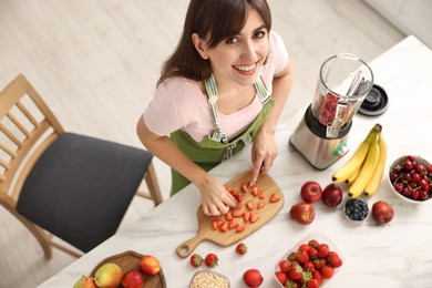 Young woman making delicious smoothie with blender at white marble table in kitchen, above view