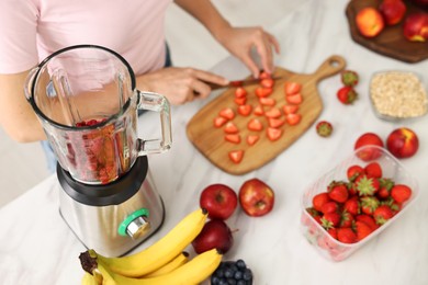 Photo of Woman making delicious smoothie with blender at white marble table in kitchen, above view