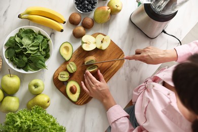 Woman making delicious smoothie with blender at white marble table in kitchen, top view