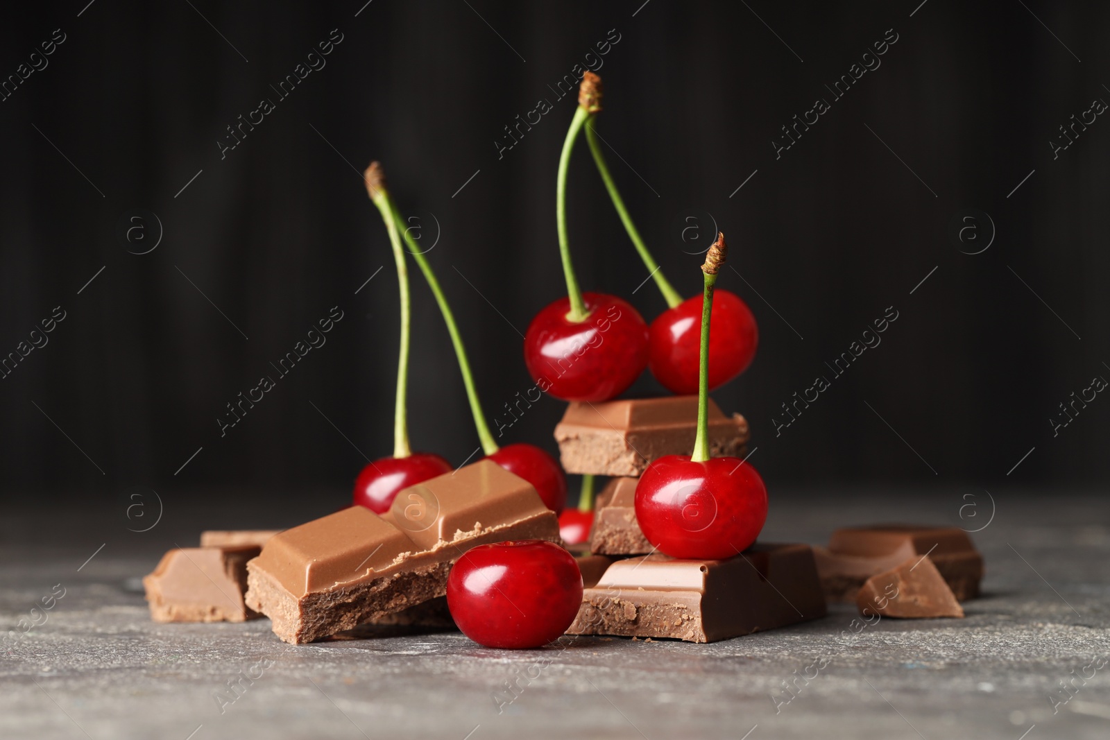 Photo of Fresh cherries with pieces of milk chocolate on grey textured table, closeup