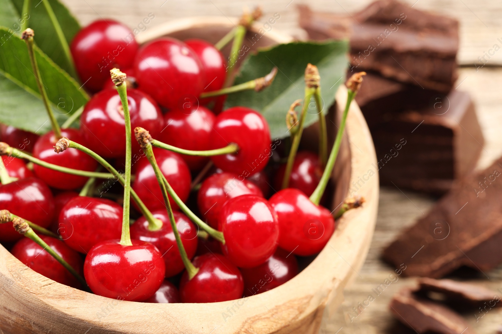 Photo of Fresh cherries with green leaves in bowl on table, closeup