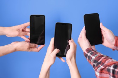 Photo of Women holding smartphones with blank screens against light blue background, closeup. Mockup for design