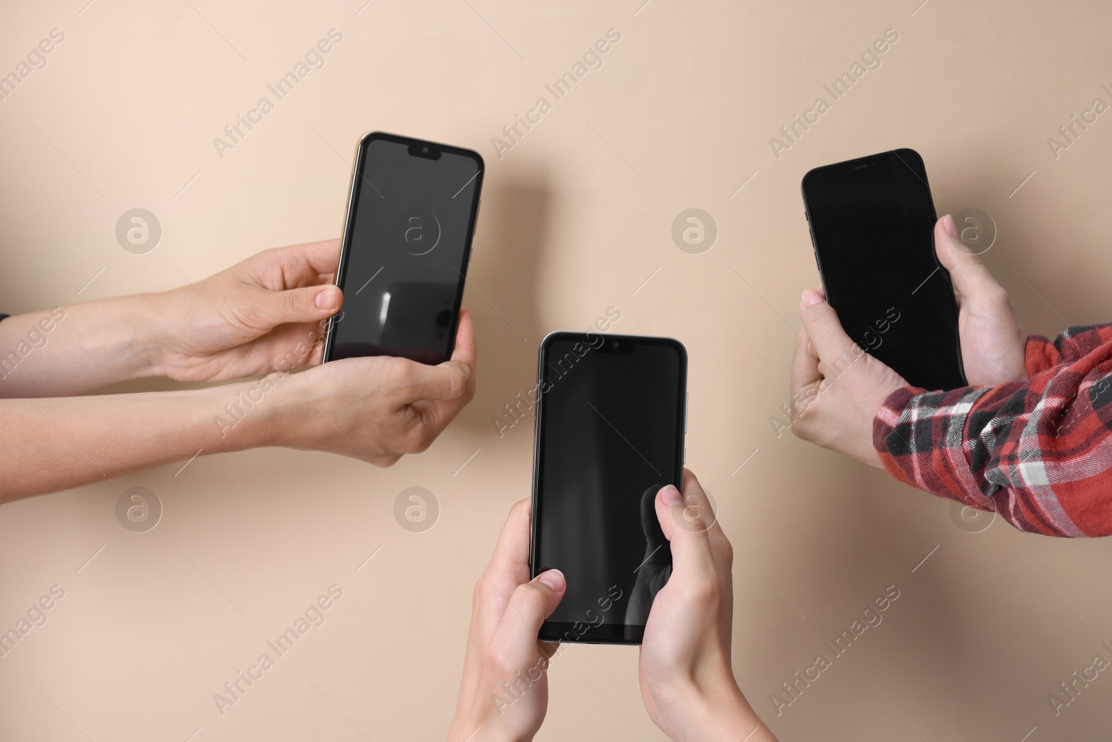 Photo of Women holding smartphones with blank screens against beige background, closeup. Mockup for design