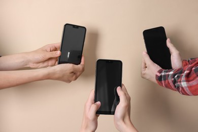 Photo of Women holding smartphones with blank screens against beige background, closeup. Mockup for design