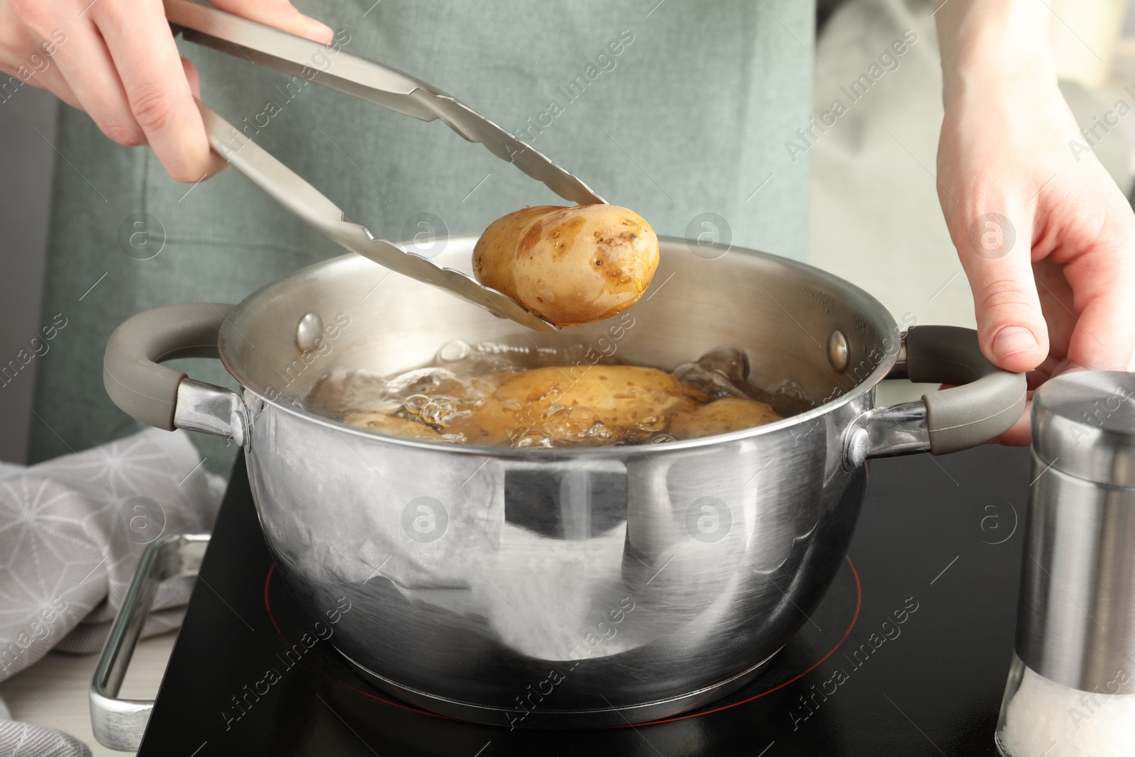 Photo of Woman putting raw potato into pot on stove, closeup