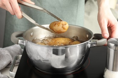 Photo of Woman putting raw potato into pot on stove, closeup