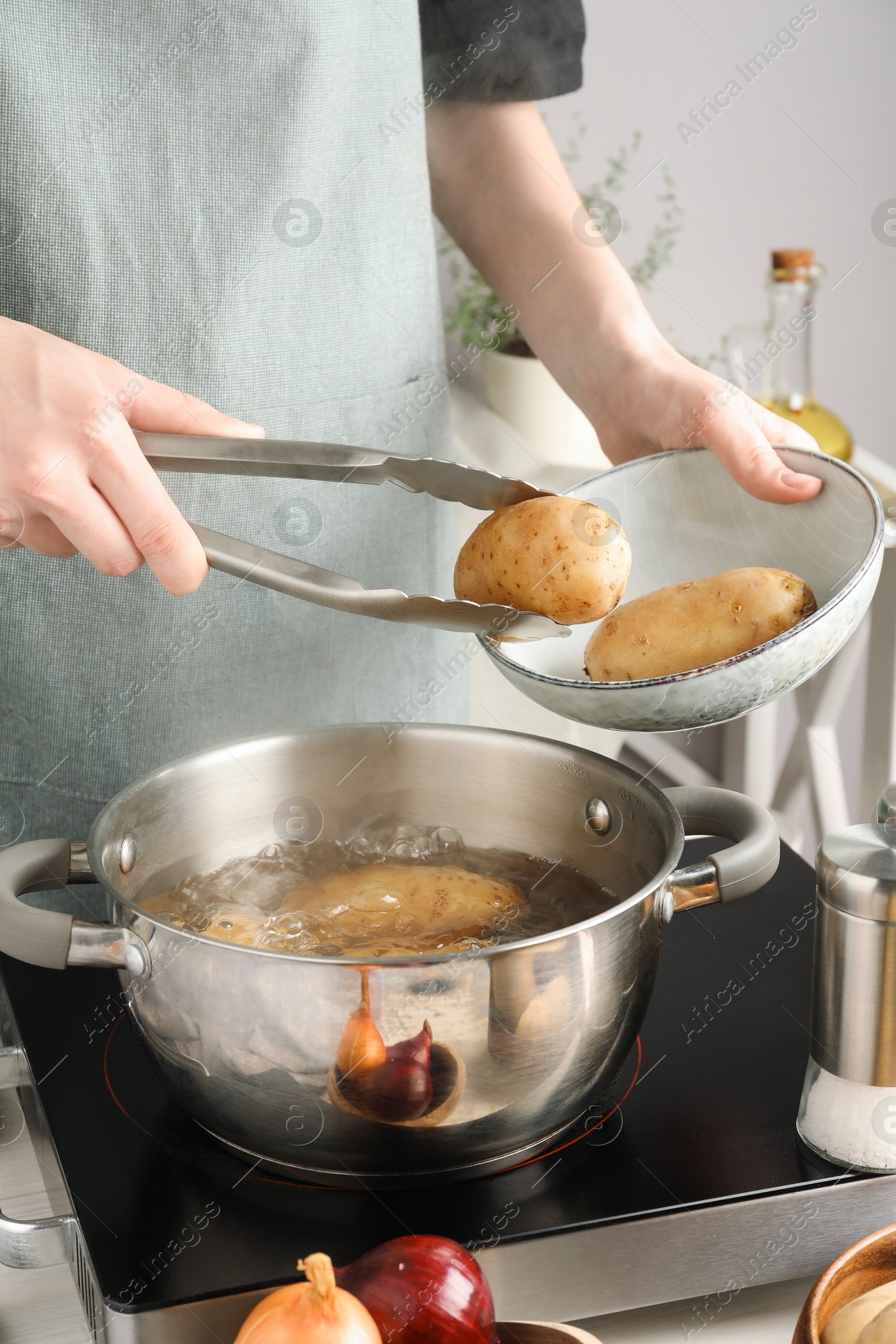 Photo of Woman putting raw potato into pot on stove, closeup