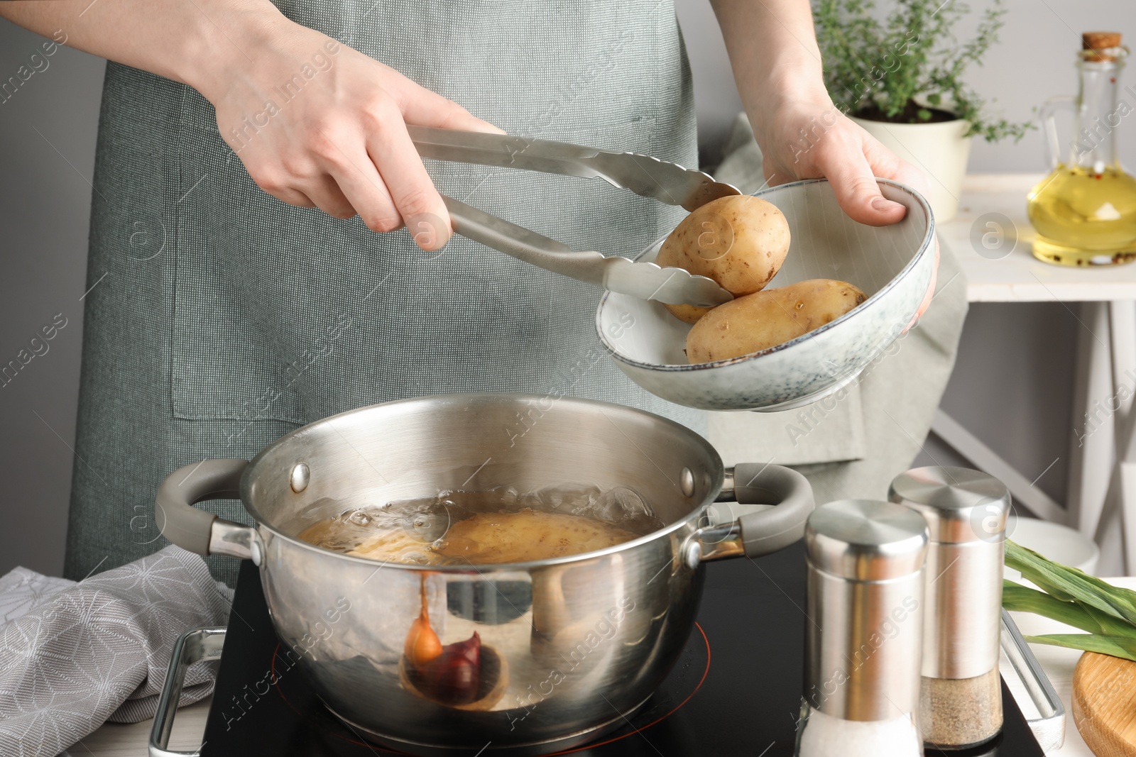 Photo of Woman putting raw potato into pot on stove, closeup