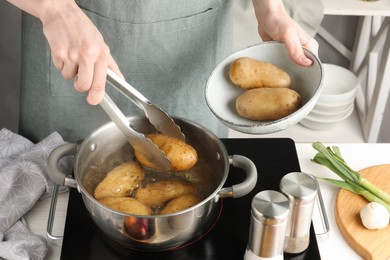 Photo of Woman putting raw potato into pot on stove, closeup