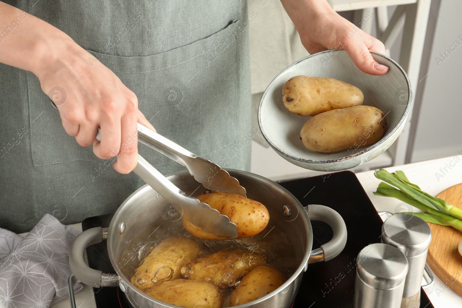 Photo of Woman putting raw potato into pot on stove, closeup