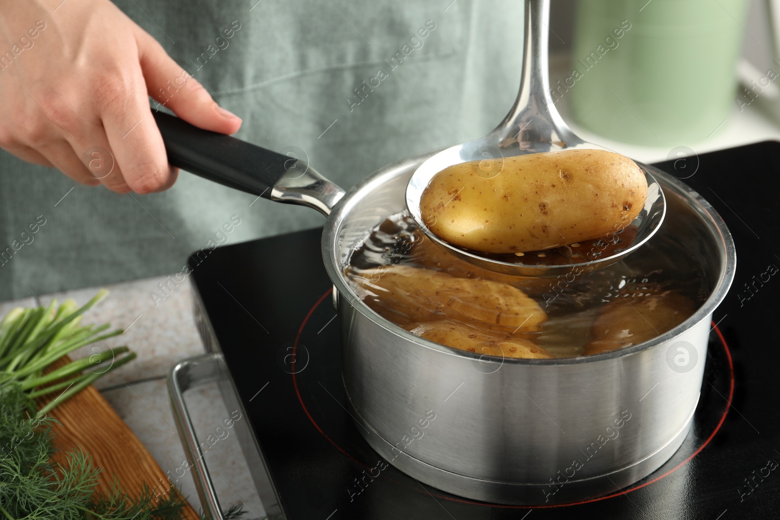 Photo of Woman taking boiled potato from saucepan on stove, closeup