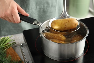 Photo of Woman taking boiled potato from saucepan on stove, closeup