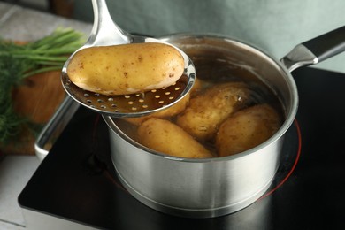 Photo of Woman taking boiled potato from saucepan on stove, closeup