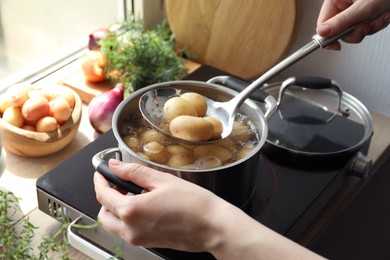 Photo of Woman taking boiled potato from pot on stove, closeup