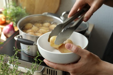 Photo of Woman taking potato from bowl at table, closeup