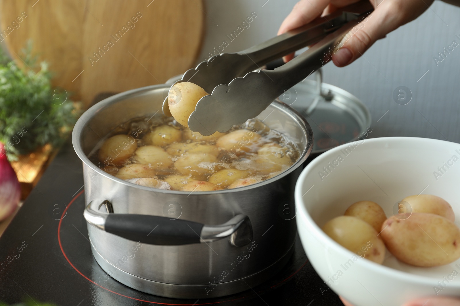 Photo of Woman putting potato into pot on stove, closeup