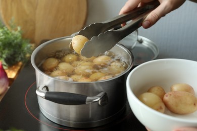 Woman putting potato into pot on stove, closeup