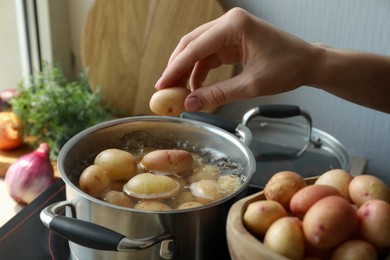 Woman putting potato into pot on stove, closeup