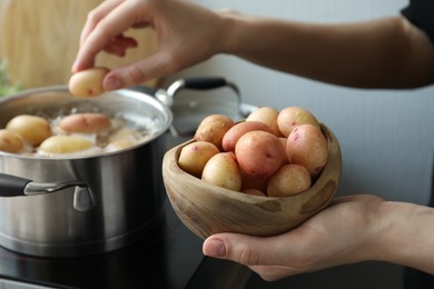 Photo of Woman putting potato into pot on stove, closeup