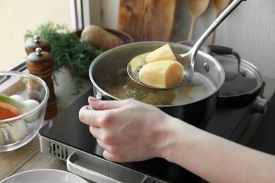 Woman taking boiled potato from pot on stove, closeup