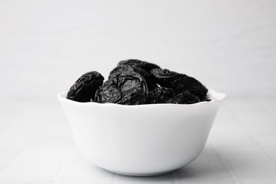 Photo of Tasty dried plums (prunes) in bowl on white tiled table, closeup