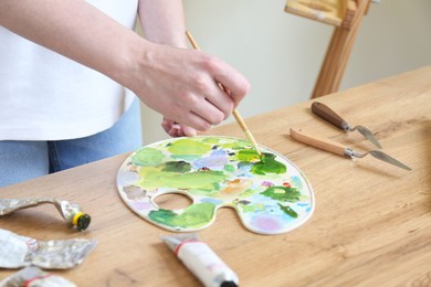 Woman with brush, palette and paints at wooden table, closeup