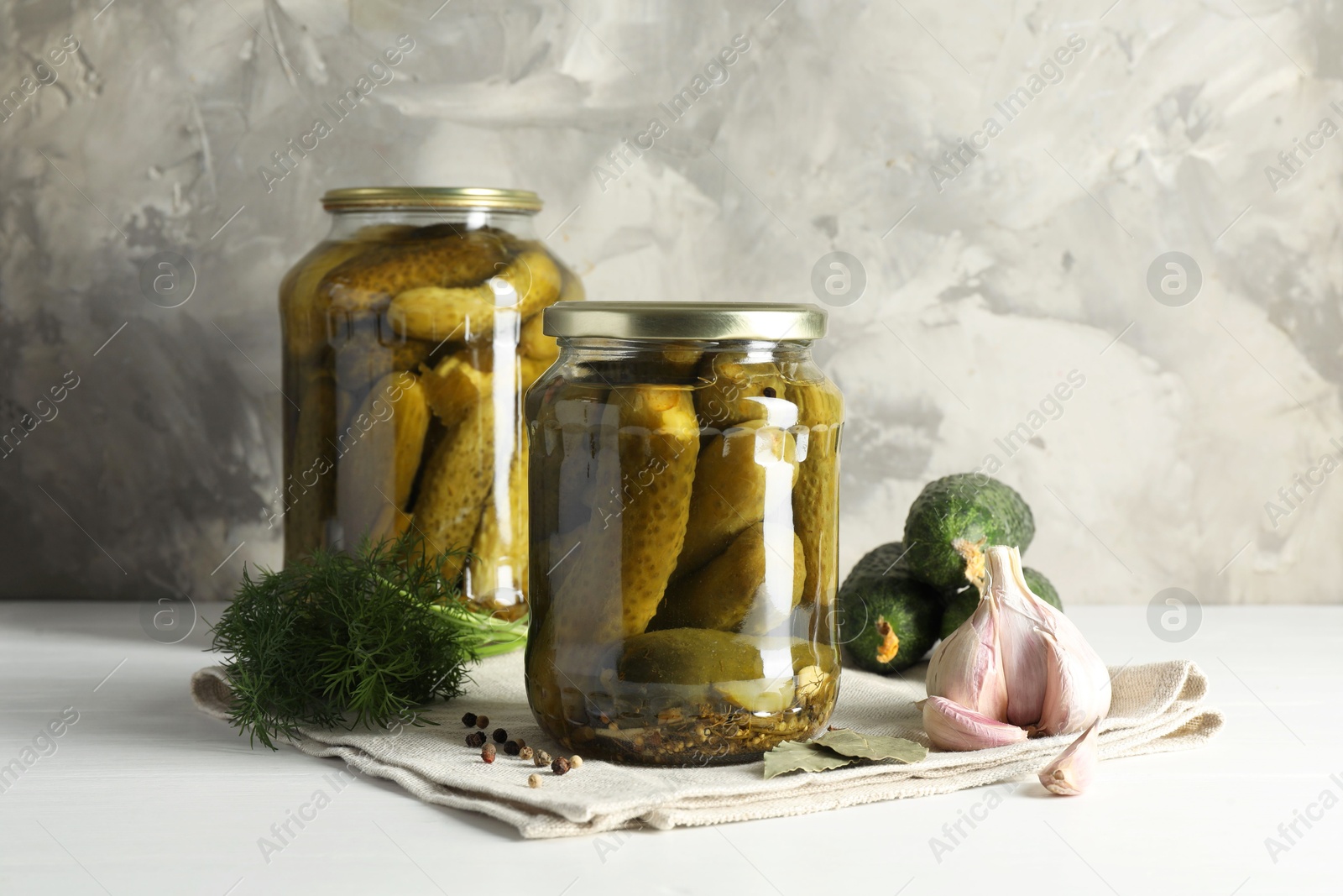 Photo of Pickles in jars, fresh cucumbers and spices on white table