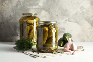 Pickles in jars, fresh cucumbers and spices on white table