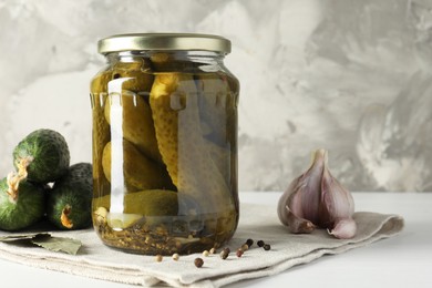 Pickles in jar, fresh cucumbers and spices on white table