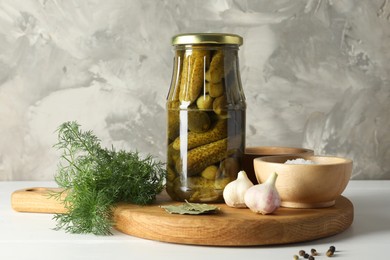 Pickled cucumbers in jar and spices on white table