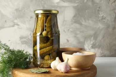 Pickled cucumbers in jar and spices on white table