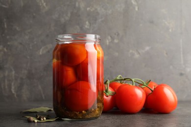 Photo of Tasty pickled tomatoes in jar, bay leaves, peppercorns and fresh vegetables on grey table