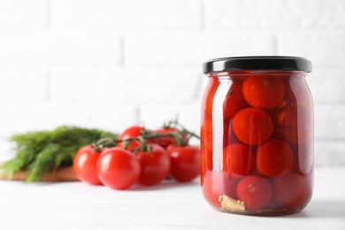 Tasty pickled tomatoes in jar and fresh vegetables on white table