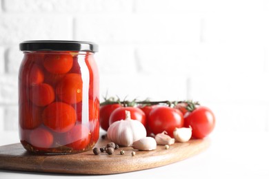 Tasty pickled tomatoes in jar, fresh vegetables and spices on white table. Space for text