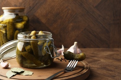 Photo of Pickled cucumbers in open jar, fork and spices on wooden table. Space for text