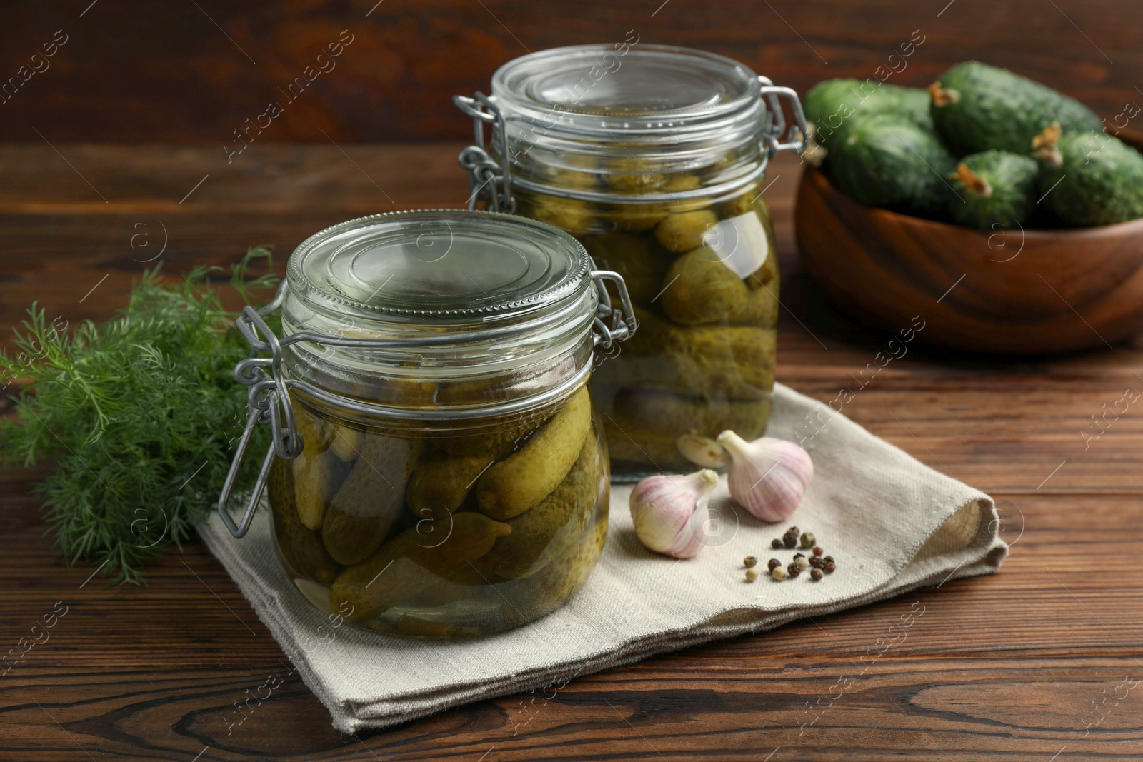 Photo of Pickled cucumbers in jars, garlic, dill and peppercorns on wooden table