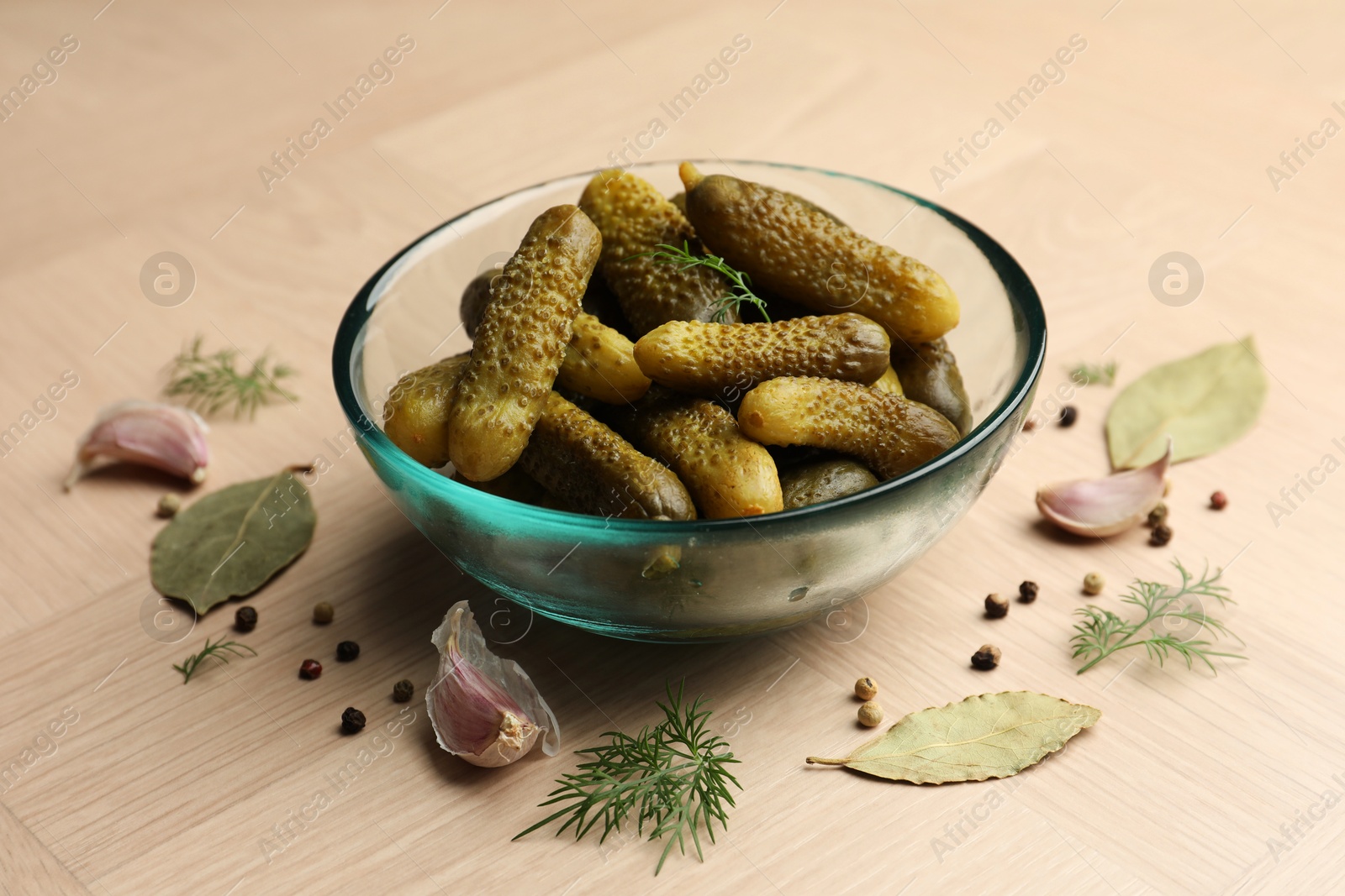 Photo of Pickled cucumbers in bowl and spices on light wooden table