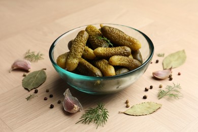 Pickled cucumbers in bowl and spices on light wooden table