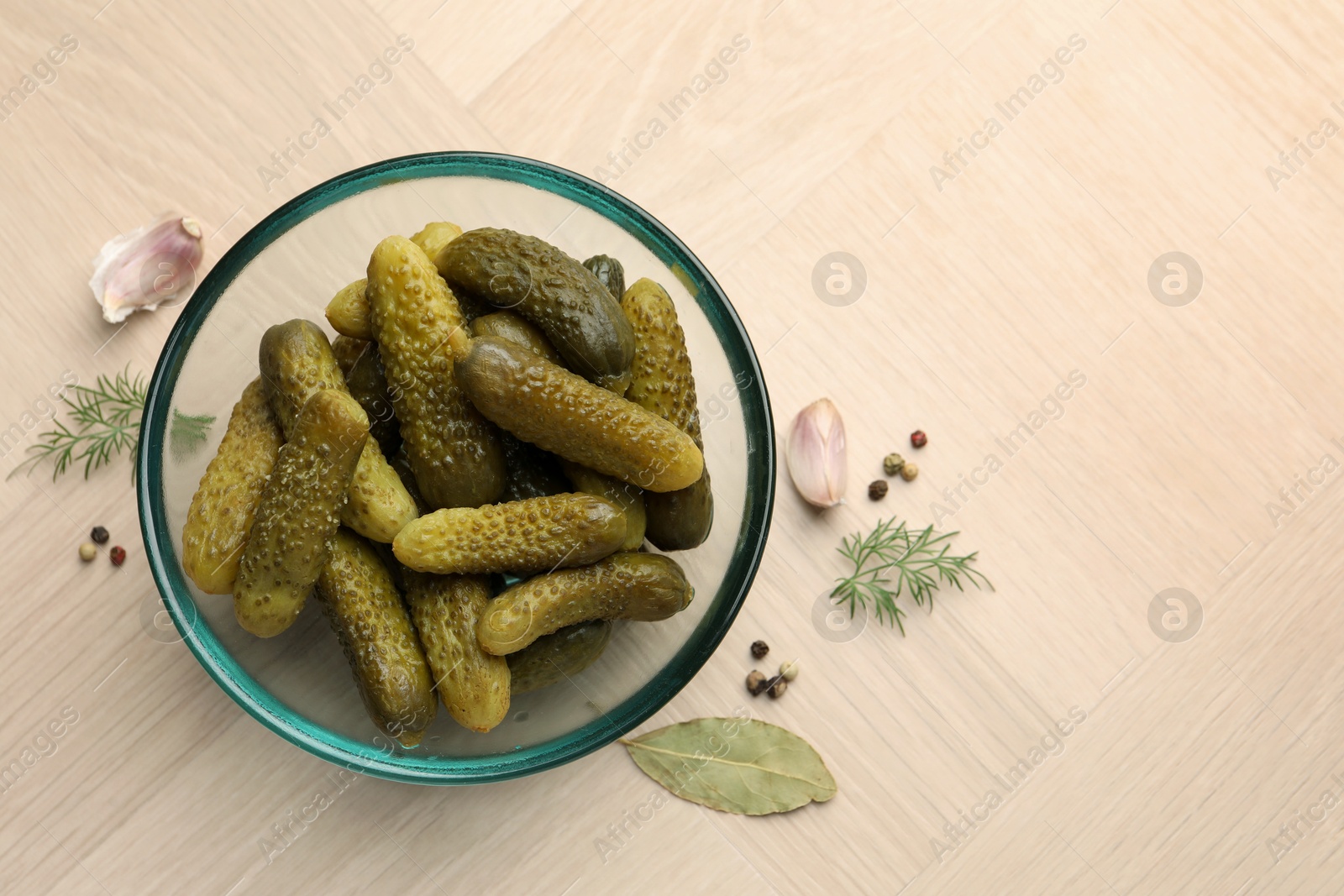 Photo of Pickled cucumbers in bowl and spices on light wooden table, flat lay. Space for text