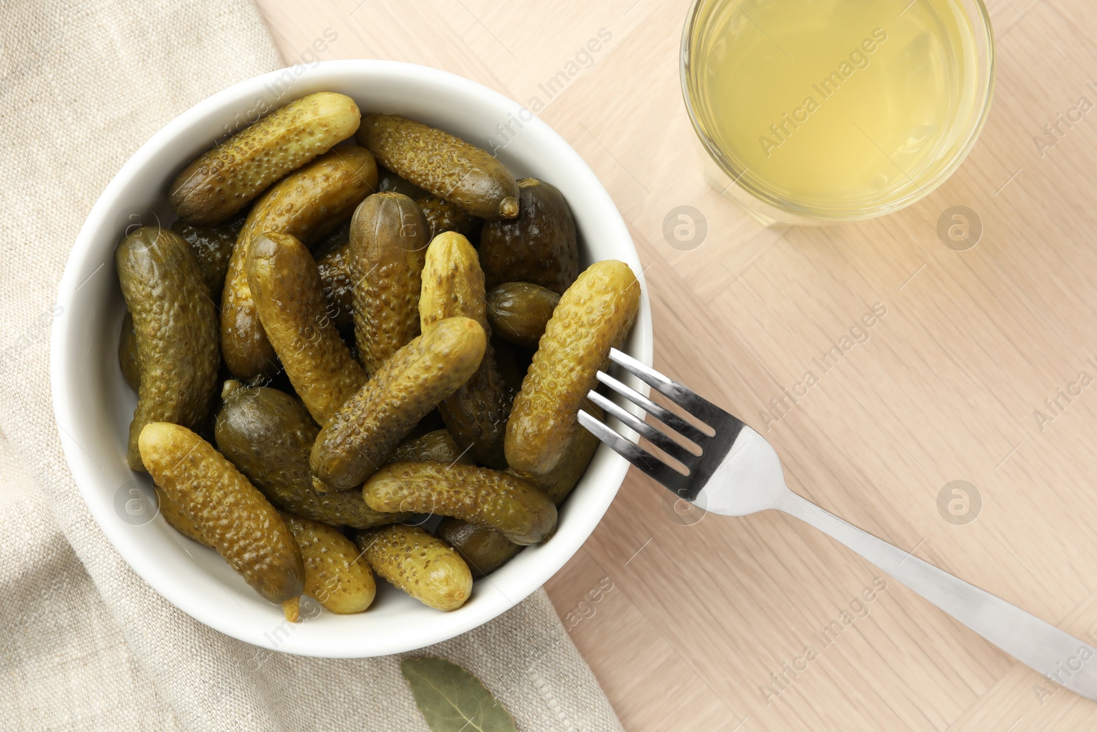 Photo of Pickled cucumbers in bowl, fork and brine on wooden table, flat lay