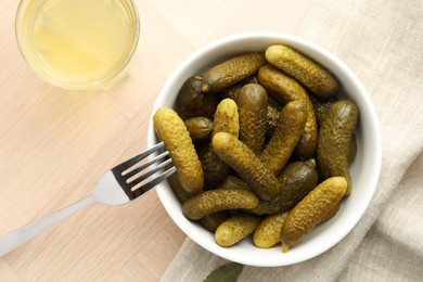 Pickled cucumbers in bowl, fork and brine on wooden table, flat lay