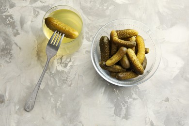 Photo of Pickled cucumbers in bowl, fork and brine on grey textured table, flat lay