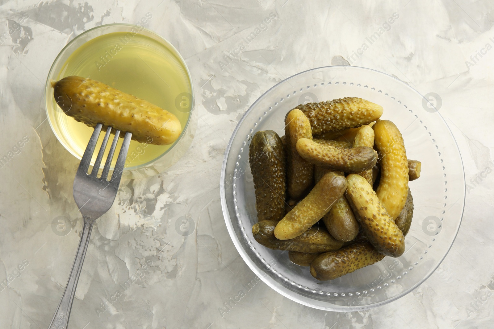 Photo of Pickled cucumbers in bowl, fork and brine on grey textured table, flat lay