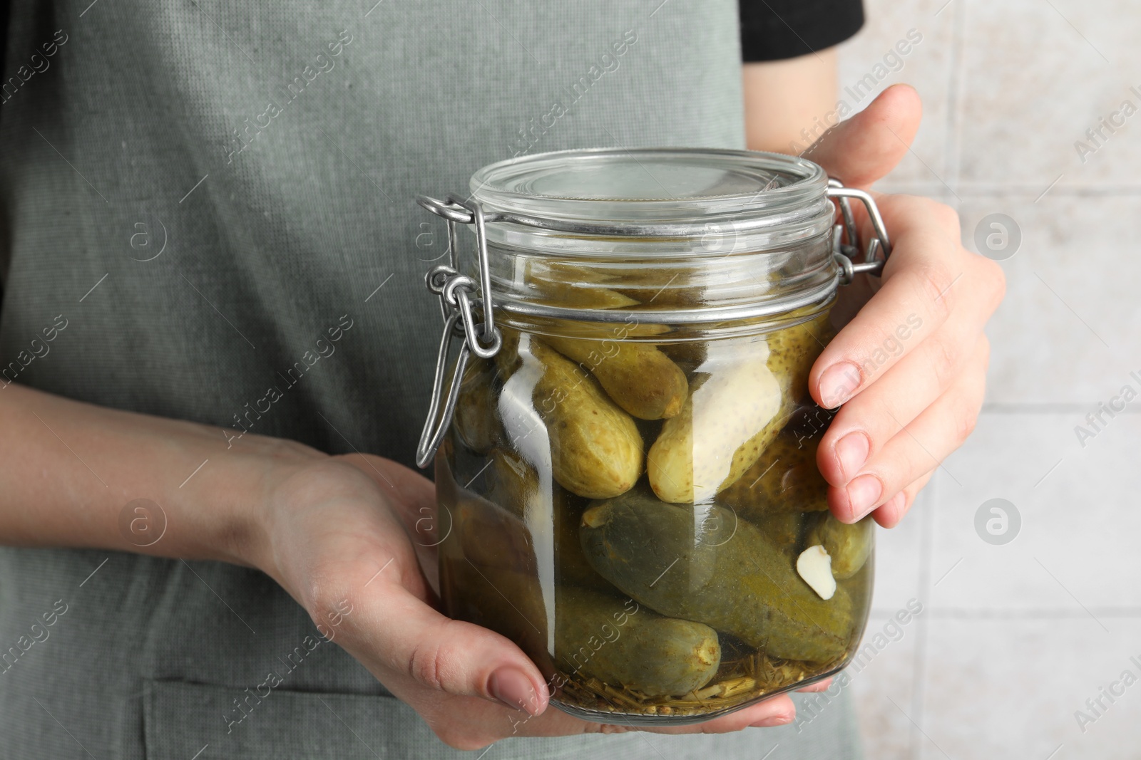 Photo of Woman holding jar with pickled cucumbers indoors, closeup