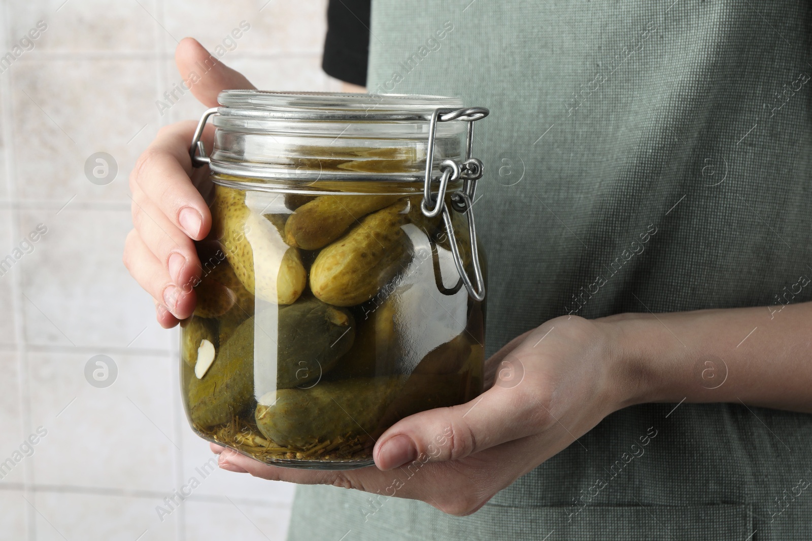 Photo of Woman holding jar with pickled cucumbers indoors, closeup