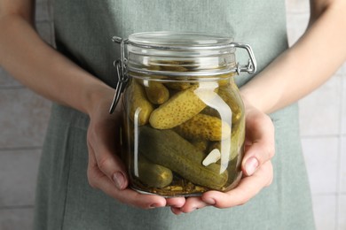 Woman holding jar with pickled cucumbers indoors, closeup