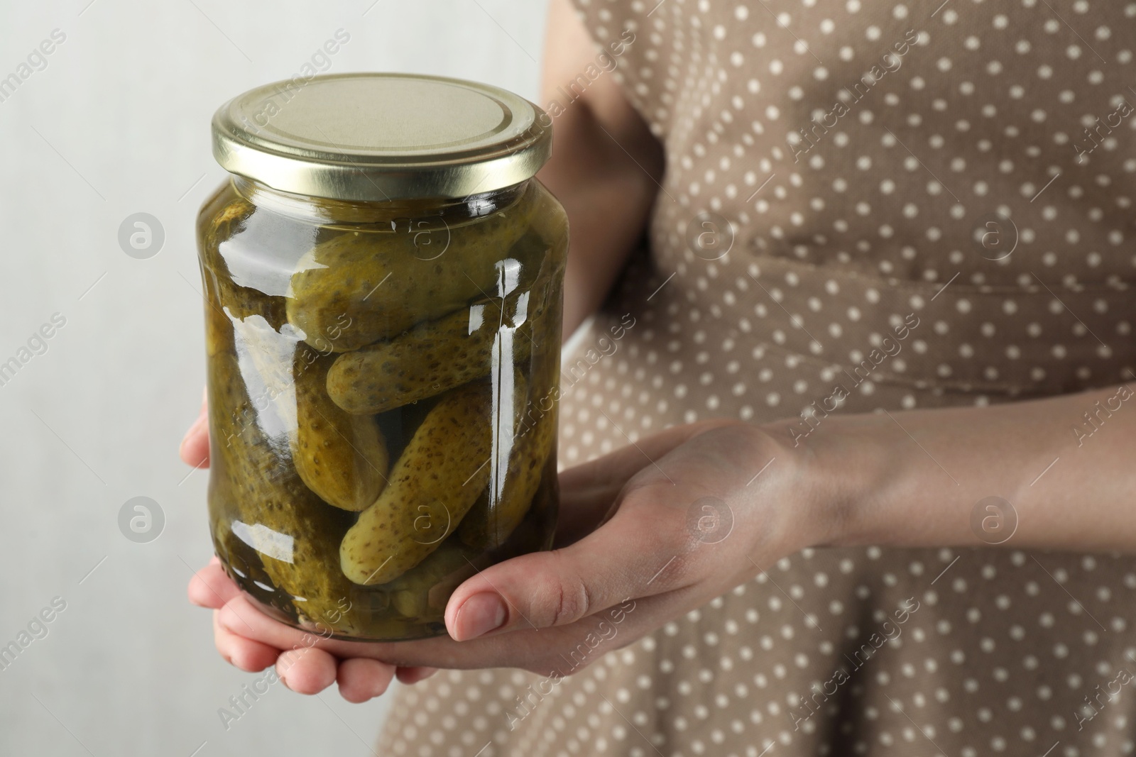 Photo of Woman holding jar with pickled cucumbers on grey background, closeup