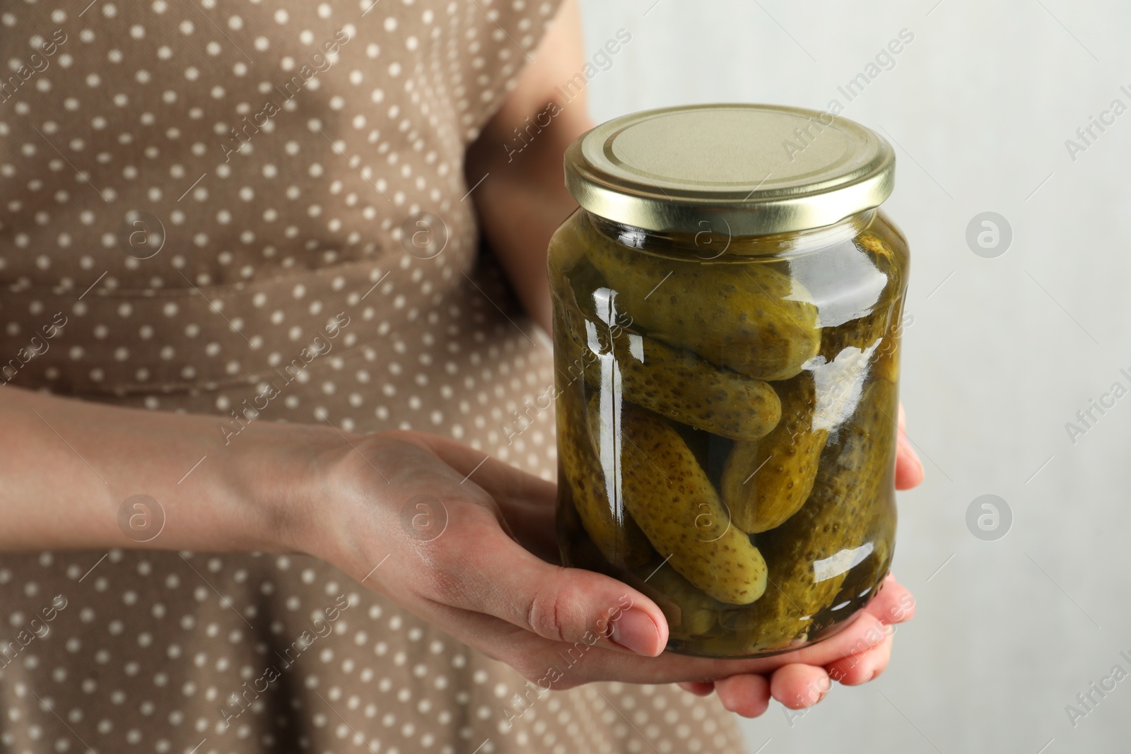 Photo of Woman holding jar with pickled cucumbers on grey background, closeup