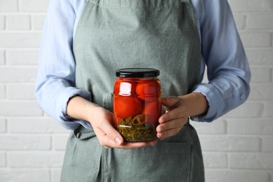 Woman holding jar with tasty pickled tomatoes against white brick wall, closeup